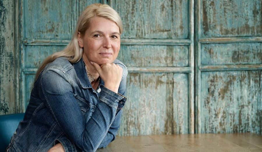Portrait image of Ilse sitting at a table. She uses SpeediCath Compact Female to manage her bladder symptoms. 