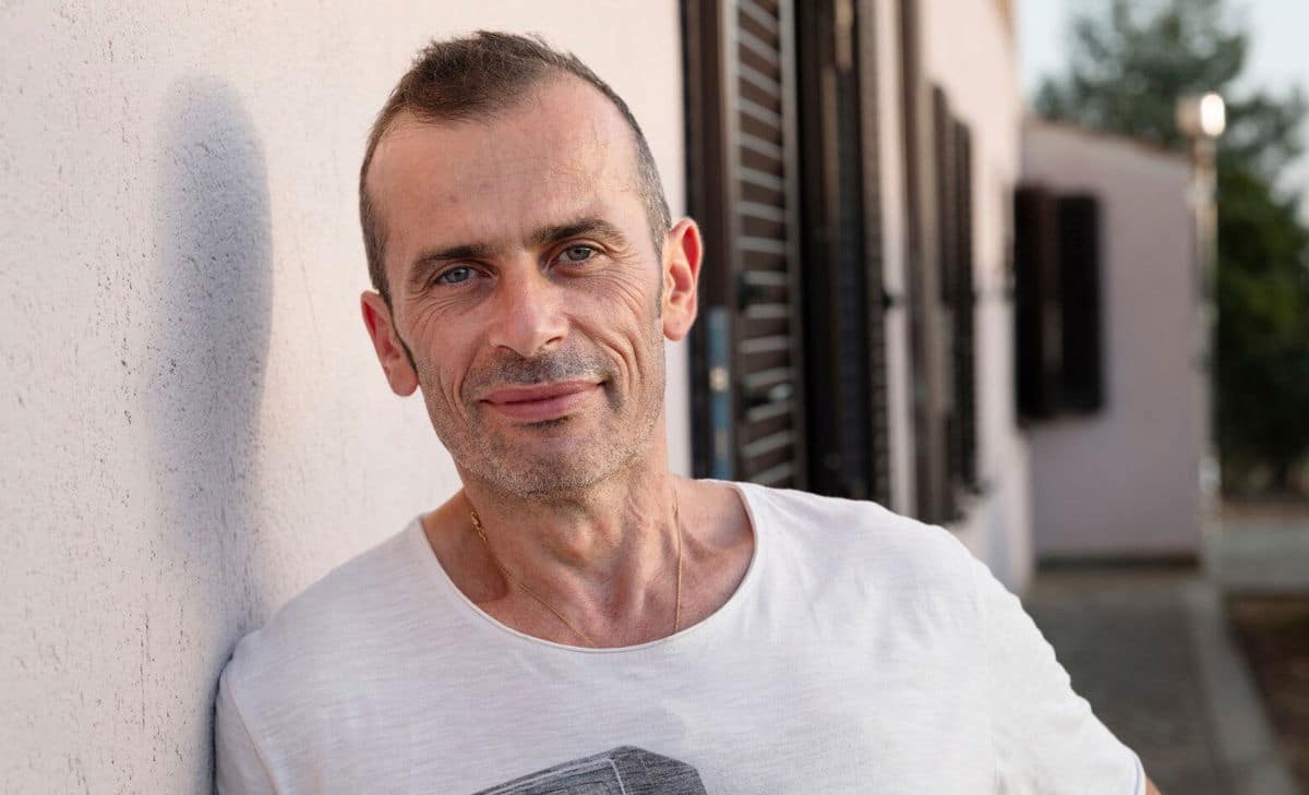 Portrait photo of Andrea stood outside his house. Andrea lives with MS and wishes he had known a little more about what to expect with the associated bladder and bowel issues.  
