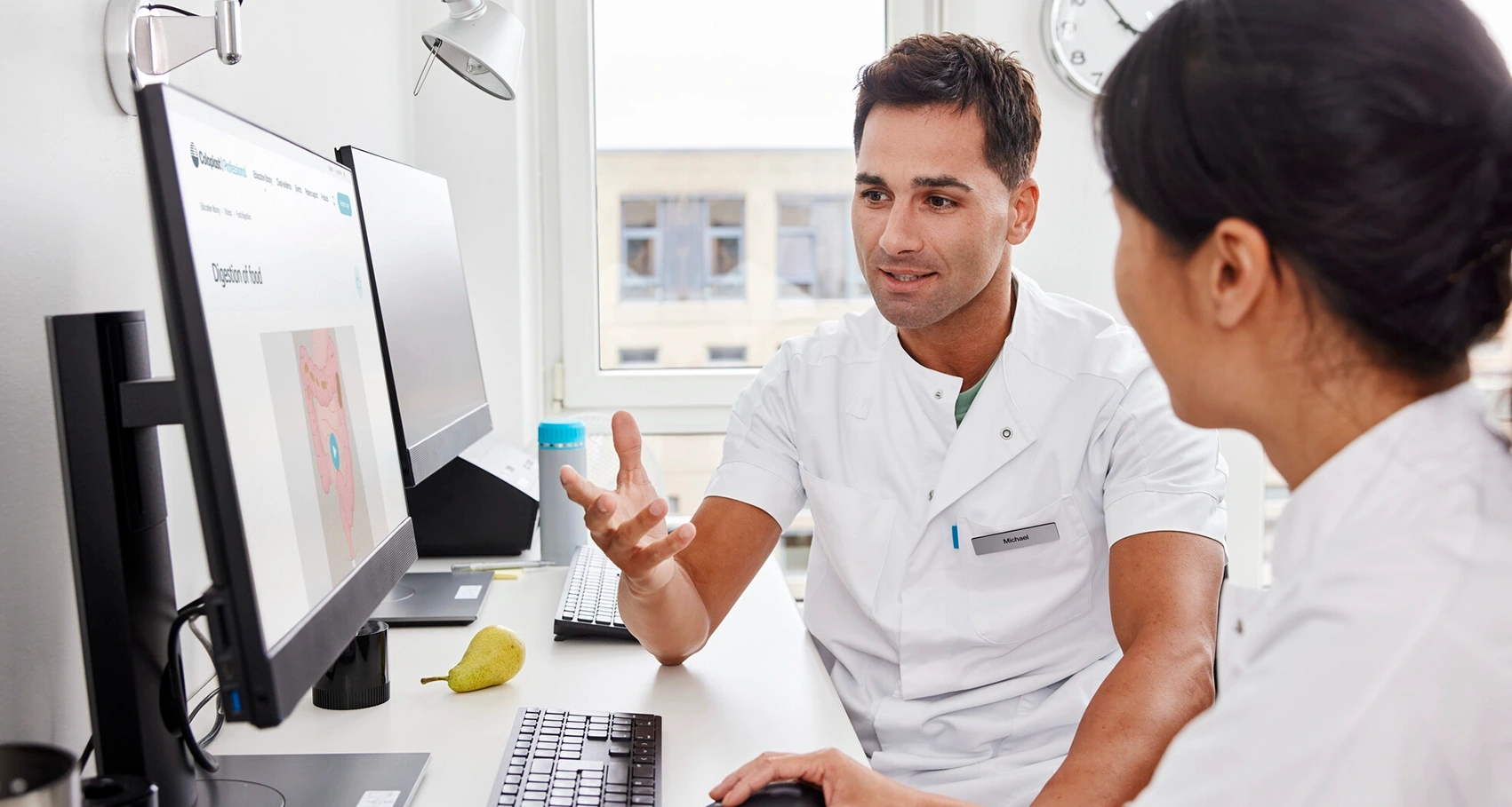 Photo of two HCPs sitting at a computer. Multiple Sclerosis can cause bowel dysfunctions. There are multiple treatment interventions that can be used to treat and manage symptoms 